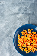 diced fresh carrots in blue plate on gray concrete background. copy space. overhead view