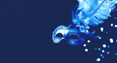 Festive mask with decorative feathers on blue background. Monochrome composition.Mardi Gras...