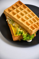 fried waffle with cheese, caramelized onions, bacon and ham on a black plate