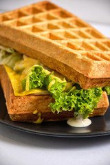 fried waffle with cheese, caramelized onions, bacon and ham on a black plate