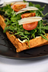 fried waffle with chicken, herbs, tomatoes, cheese, balsamic vinegar on a black plate
