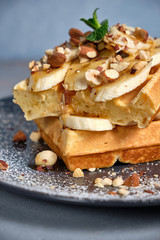 Sweet waffle with caramel and bananas sprinkled with hazelnuts and icing sugar