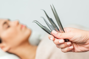 Cosmetologist holds tweezers for eyelash extensions on background of patient, close up.