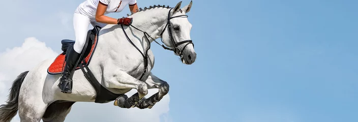 Fotobehang Meisje springen met wit paard, geïsoleerde, blauwe lucht, witte wolken achtergrond. Ruiter in wit uniform, paardensport. Horizontale koptekst of banner. Ambitie, doorbreken, gratis, gezondheidsconcept. © taylon