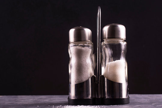 Glass salt shaker and sugar bowl on a dark background. Free space for an inscription.