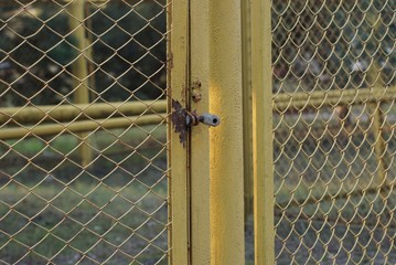 part of an iron yellow fence made of metal mesh on a pole and a gray padlock on a door