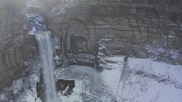 Tall waterfall flowing over rocky cliff in gorge on winter day. Aerial 4K drone footage.