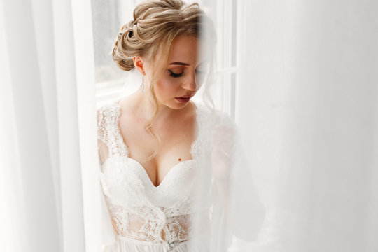 portrait a sexy blonde woman in underwear near big window . morning of  beautiful bride in hotel room with stylish white interior. young womans face with attractive neckline in white  dress close up.