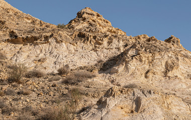 Fototapeta na wymiar a steep rocky hillside in the judean desert mountains above near ein mabo'a in the west bank showing exposed layers of limestone, chalk, flint and sparse vegetation