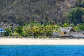 A distant view on a fishing cottage, located on a seashore of a small island next Flores, Indonesia. Clear, turquoise coloured water displaying coral reef. Solitude and calmness. Simple construction