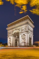 Fototapeta na wymiar Arc de Triomphe at dusk in Paris in France with traffic of cars light trails and yellow leafs moved by the wind