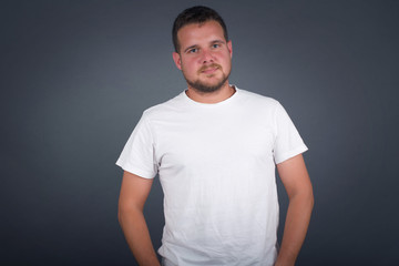 Confidence and business concept. Portrait of charming successful young man, smiling broadly with self-assured expression while holding hands in pockets standing against gray wall.