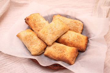 Homemade freshly baked puff pastry pies stuffed with mushrooms and eggs sprinkled with sesame seeds on white parchment. Delicious appetizer.