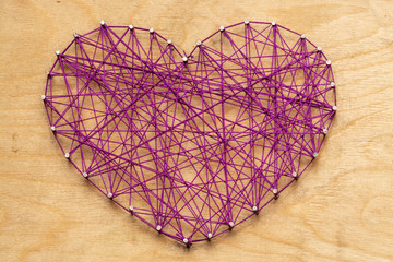 The heart is made of purple threads wrapped on nails embedded in a wooden board. View from above