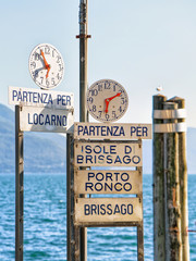 Clock at the Pier at the promenade at Ascona luxurious resort on Lake Maggiore, of Ticino canton in Switzerland. The lettering on the sings under the clocks are Names of towns and their piers on the