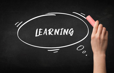 Hand drawing LEARNING inscription with white chalk on blackboard, education concept