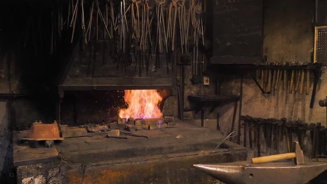 Oscura fragua con el fuego encendido junto a yunque y martillo de cerrajero