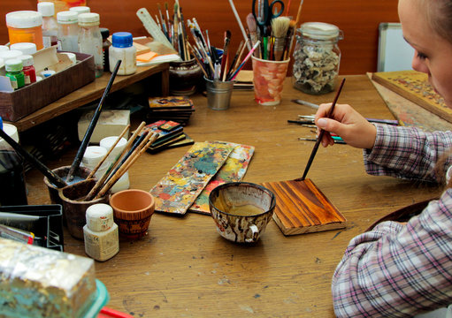 Process Of Aging Of A Wooden Picture, Processing Of Wood, Toning With Wood Stain. Girl Artist Paints A Picture In The Studio. Brushes And Paints On The Background.