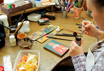 Artist brush taken a paint. Girl artist paints a picture in the studio. Reproduction of the icon of St. Nicholas. Workflow of the artist in the studio. Brushes and paints on the background.