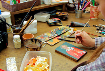 Artist paints a picture of acrylic paints. Close-up view. Artist's desktop. Reproduction of the icon of St. Nicholas. Workflow of the artist in the studio. Brushes and paints on the background
