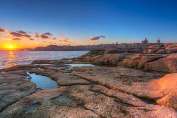 Rocky coastline of Malta and beautiful architecture of the Valletta city at sunrise