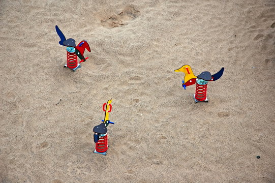 Drei Federwippen in rot, gelb und blau im Sand, Kinderspielplatz