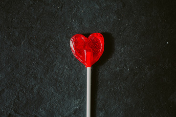 Close up view of red heart shaped lollipop on black slate background. 