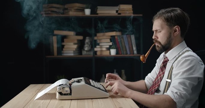 Focused middle-aged male writer smoking pipe and working on new book, vintage