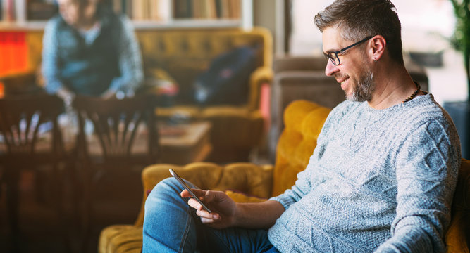 Middle-aged man working on mobile phone, sitting at the cafeteria, lifestyle concept