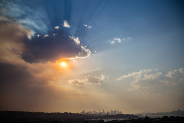 Clouds and orange smoke from the bushfires cover the sun and the skyline of Sydney with the Harbour Bridge in the background.