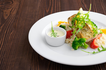 Closeup view of fried zander with rice, bell pepper and arugula served with mayonnaise sauce on dark wooden background