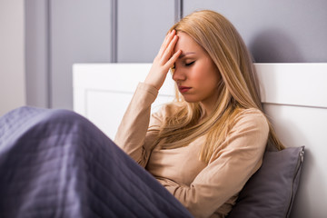 Woman having strong headache while sitting in bedroom.	