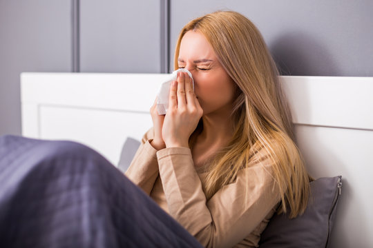 Exhausted woman having fever and blowing nose.	