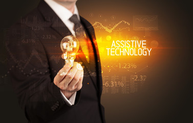 Businessman holding lightbulb with ASSISTIVE TECHNOLOGY inscription, Business technology concept