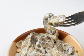 Mushrooms fried in milk on a fork over a plate on white background