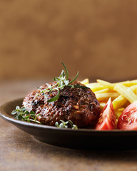 Hamburger steak with french fries and tomatoes. Brown stone background. Close up.
