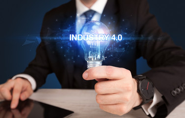 Businessman holding light bulb with INDUSTRY 4.0 inscription, innovative technology concept