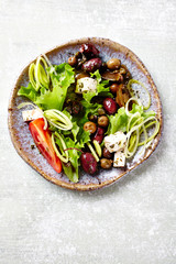 Healthy salad with various olives, feta cheese, tomatoes and lettuce. Bright wooden background. Top view. 