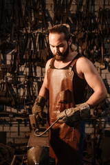 Fototapeta na wymiar Brutal muscular blacksmith in a dark workshop forges iron. Vertical photo