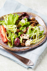 Healthy salad with various olives, feta cheese, tomatoes and lettuce. Bright wooden background.