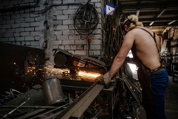 Obraz na płótnie Canvas Brutal bearded man craftsman, saws metal at the factory