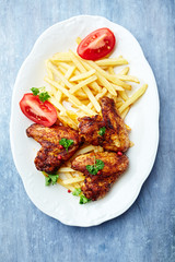 Spicy chicken wings with french fries and tomatoes. Bright wooden background. Top view.