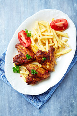 Spicy chicken wings with french fries and tomatoes. Bright wooden background. Top view. 
