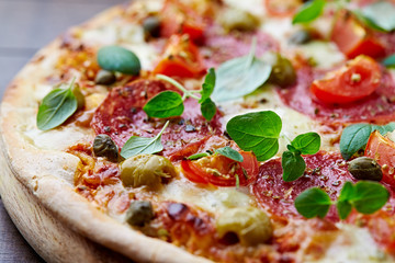  Pizza with salami, green olives, mozzarella cheese, capers and fresh basil. Brown wooden background