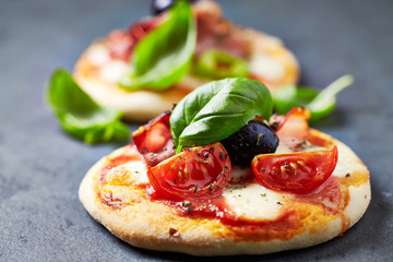 Mini pizzas with ham, mozzarella cheese, black olives and fresh basil on dark stone background. Close up.