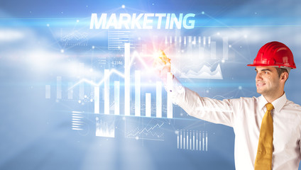 Handsome businessman with helmet drawing MARKETING inscription, architecture business plan concept