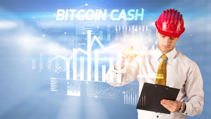 Handsome businessman with helmet drawing BITCOIN CASH inscription, architecture business plan...