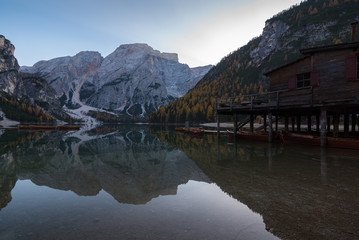 Fototapeta na wymiar Typical scenery of Braies Lake Pragser Wildee duuring autumn with water reflections boats mountains hut trees foliage
