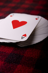 Full deck of playing cards with ace of hearts on top lying on checkered plaid. Vertical photo. Place for text