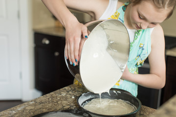 young girl pouring cake batter into pan - obrazy, fototapety, plakaty
